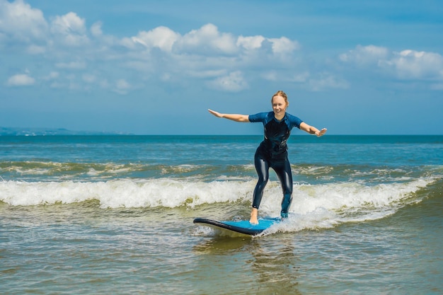 Radosna młoda kobieta początkujący surfer z niebieskimi falami bawi się na małych falach morskich. Aktywny styl życia rodziny, ludzie lekcja sportów wodnych na świeżym powietrzu i aktywność pływania na letnich wakacjach na obozie surfingowym.