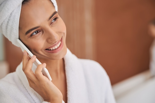 Radosna młoda kobieta rozmawia przez telefon komórkowy po prysznicu