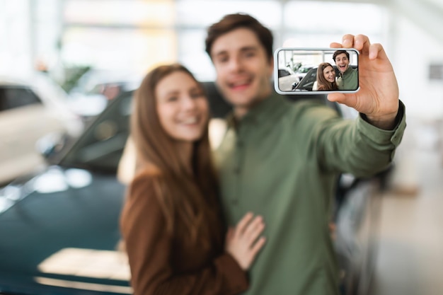 Zdjęcie radosna młoda para kaukaska robi selfie po zakupie nowego samochodu w salonie selektywnym focus