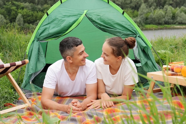 Radosna para w naturze kobieta i mężczyzna noszący zwykłe ubrania leżący w namiocie w pobliżu rzeki wesołych wakacji romantyczny weekend cieszący się komunikacją ze sobą