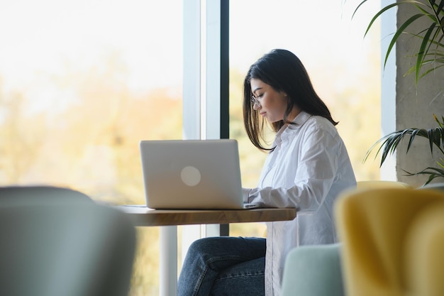 Radosna studentka studiująca online w kawiarni za pomocą laptopa i słuchawek pusta przestrzeń