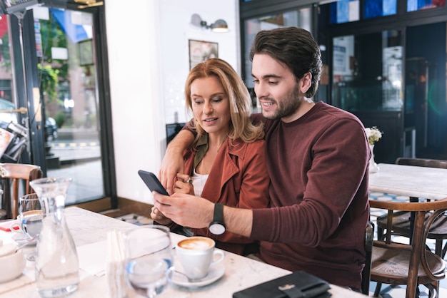 Radosna szczęśliwa para pozuje w restauracji i przy użyciu telefonu