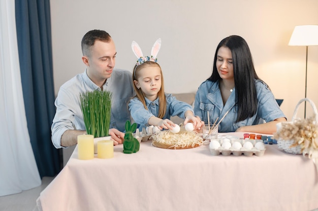 Radosne rodzinne spotkanie przy stole w nowoczesnej, lekkiej kuchni i wspólne malowanie pisanek