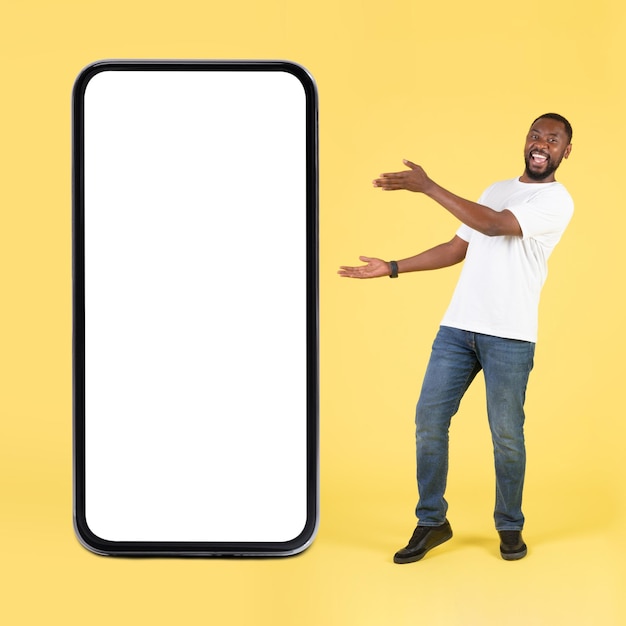Radosny czarny facet pokazujący duży ekran telefonu na żółtym tle