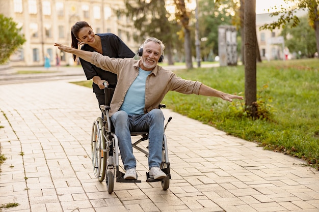 Radosny dojrzały niepełnosprawny mężczyzna na wózku inwalidzkim w słuchawkach bawiący się podczas spaceru po mieście