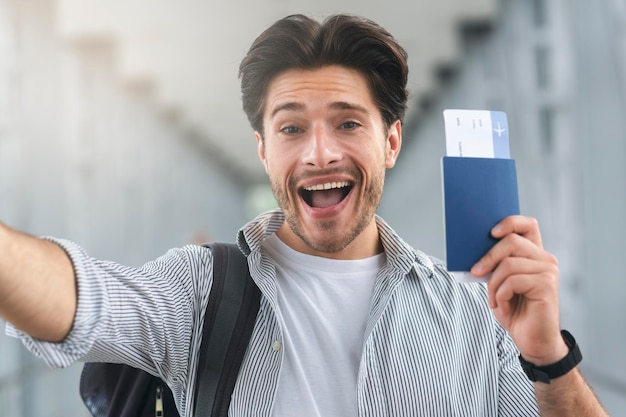 Radosny facet biorący selfie z paszportem i przepustkami na lotnisku