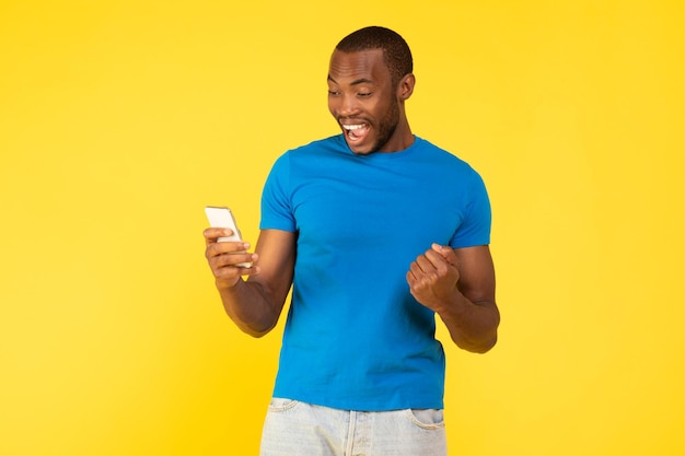 Radosny Murzyn używający smartfona gestem Tak na żółtym tle