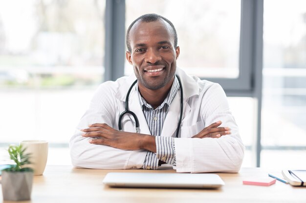 Radosny pracownik medyczny siedzi w miejscu pracy i pozowanie