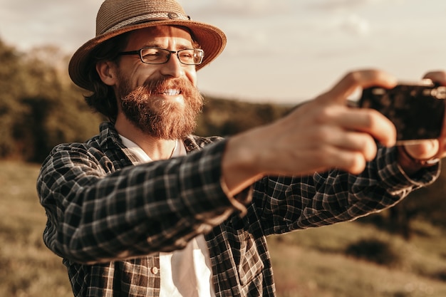 Radosny stylowy męski podróżnik robiący selfie z smartphonem