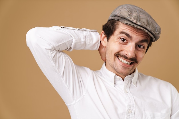 Zdjęcie radosny wąsaty mężczyzna w kapeluszu uśmiechnięty na beżowym tle