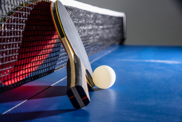 Rakieta do tenisa stołowego zbliżenie czarny i czerwony białą piłkę na niebieski stół do ping ponga z siatką, tenis stołowy wiosło to sprzęt sportowy konkurencji kryty aktywność i ćwiczenia na tle koncepcji