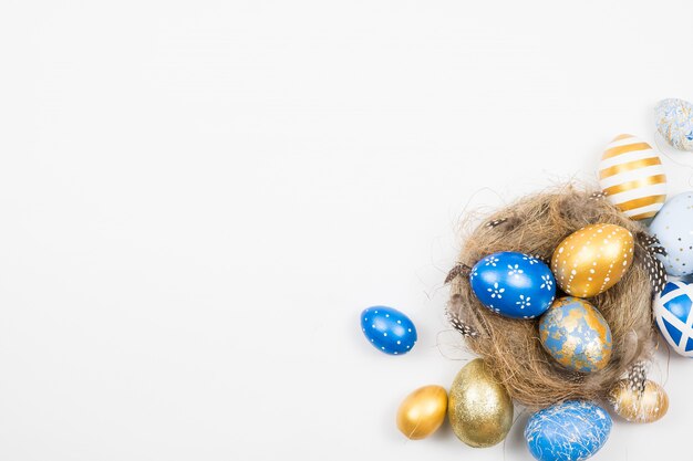 Rama Wielkanocni złoci dekorujący jajka w gniazdeczku odizolowywającym na biel powierzchni. Minimalna koncepcja wielkanocy.