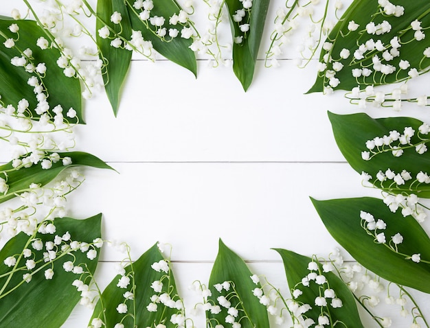 Zdjęcie rama wykonana z liści konwalii na białym drewnianym tle.