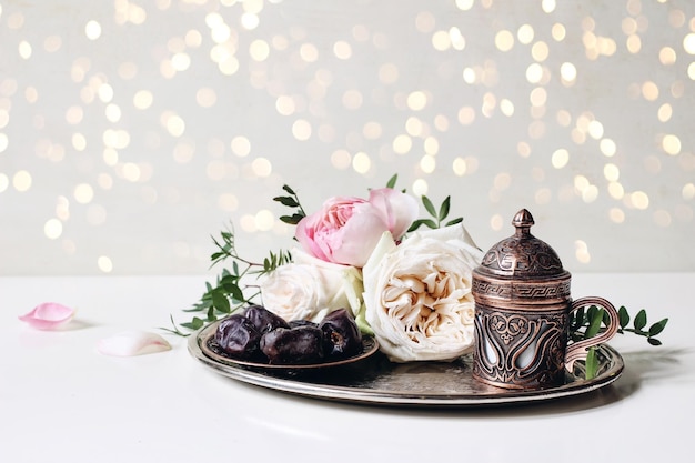 Ramadan Kareem kartkę z życzeniami zaproszenie iftar obiad muzułmański Eid ul Adha transparent płyta z datami owoce brąz filiżanka kawy różowe róże i zielone gałęzie Świąteczne światła bokeh Biały stół tło