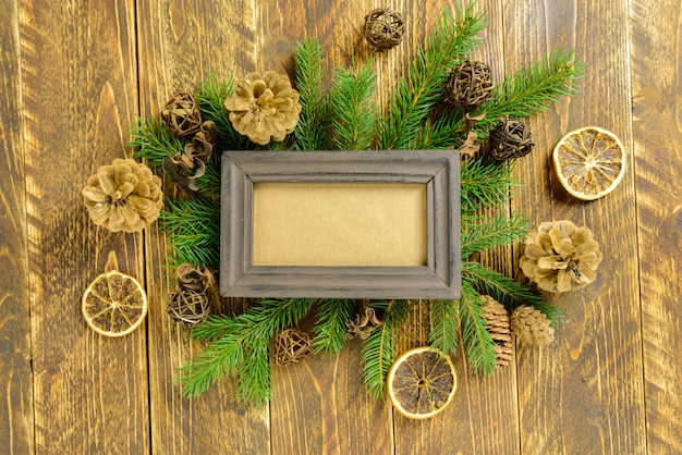 Ramka na zdjęcia między dekoracjami świątecznymi, z szyszkami na brązowym drewnianym stole. Widok z góry, ramka do skopiowania miejsca.