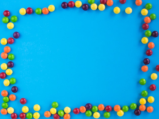 Ramka wielobarwnych małych cukierków na niebieskim tle miejsca kopiowania tekstu płasko świecki widok z góry