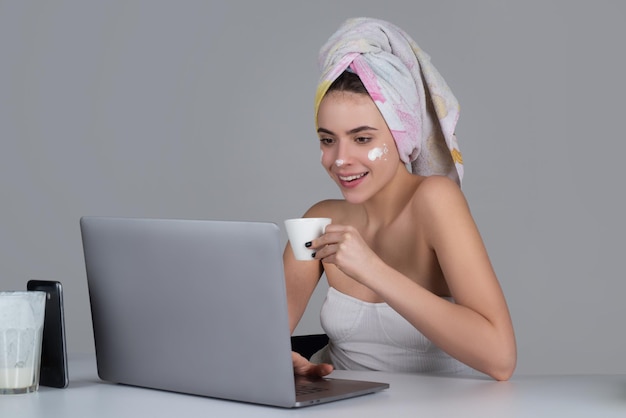 Rano kobieta z kawą i maseczką na codzienną rutynę. Cieszyć się czasem w domu. Piękna młoda uśmiechnięta kobieta pracuje na laptopie i pije kawę.