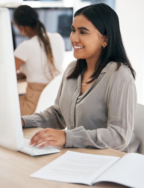 Raport komputerowy i pisanie z indyjską kobietą w biznesie pracującą na pulpicie w swoim biurze w pracy Internetowa poczta e-mail i pulpit z młodą pracownicą w pracy jako zawodowa sekretarka