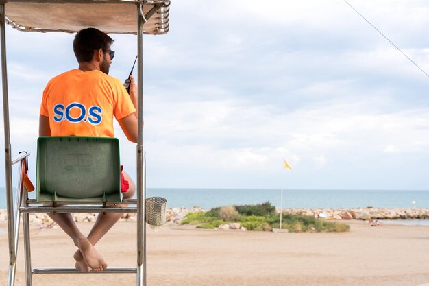 Ratownik za pomocą radia siedzi na krześle na plaży