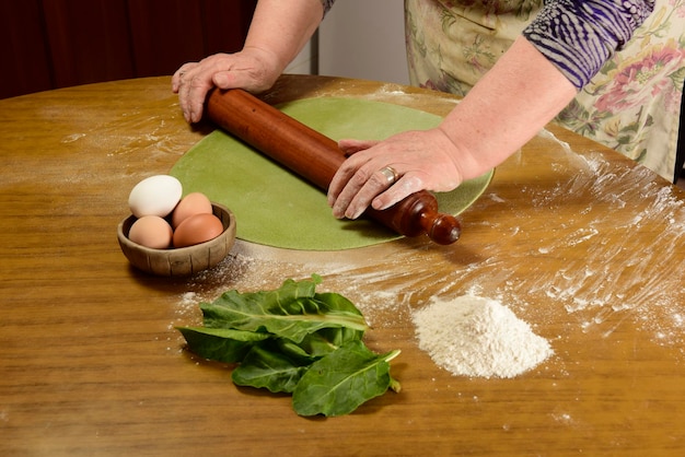 Ręce babci ugniatające ciasto na zielony makaron