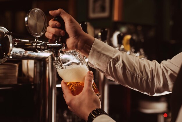 Ręce barmana wlewają do szklanki lekkiego spienionego piwa z kranu