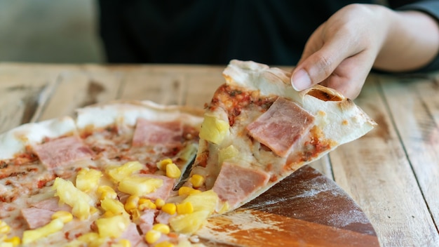 Ręce biorące plasterki domowej włoskiej pizzy na drewnianym stole