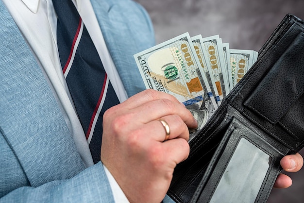 Ręce biznesmena trzymającego czarny skórzany portfel z banknotami dolarowymi