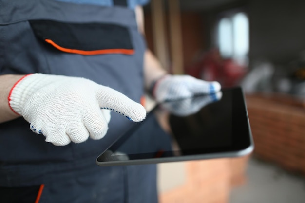 Ręce budowniczego w rękawiczkach używają tabletu do budowy i naprawy pomieszczeń