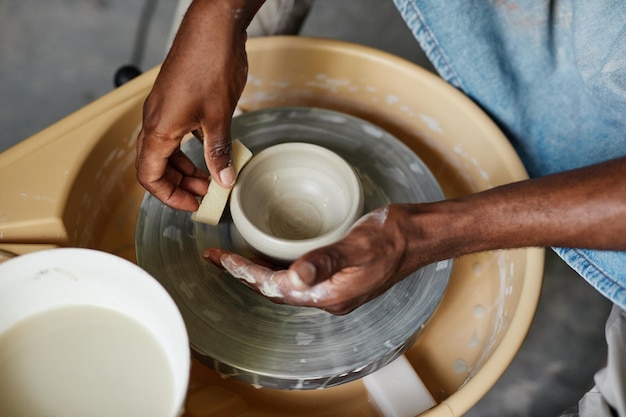 Ręce czarnego młodzieńca używającego koła garncarskiego i tworzącego ręcznie robioną ceramikę