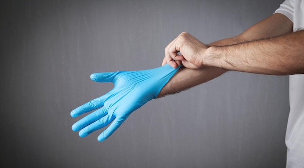 Ręce człowieka, zakładanie rękawiczek z niebieskiej gumy lateksowej.