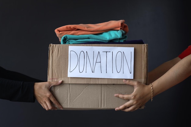 Ręce dające i odbierające pudełko z ubraniami na cele charytatywne i darowizny na ciemnoszarym tle.