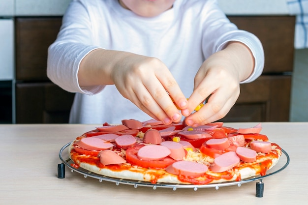 Ręce Dzieci Posypują Ser Pizzą. Proces Gotowania Domowej Pizzy Przez Dziecko. Umiejętności Przedszkolaka, Mały Pomocnik. Rodzinny Wypoczynek. Sztuczny Hałas, Selektywne Ustawianie Ostrości, Podświetlenie