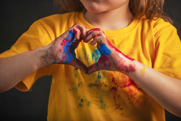 Ręce dzieci w wielobarwnych kolorach Holi pokazują znak w kształcie serca z rękami, znak miłości