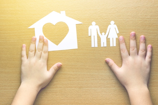 Zdjęcie ręce dzieci z małym modelu domu i rodziny na drewniane tła