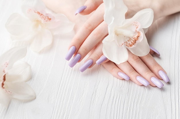 Ręce dziewczyny z delikatnym fioletowym manicure i kwiatami orchidei