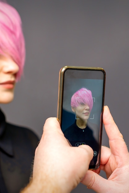 Zdjęcie ręce fryzjer człowieka biorąc zdjęcie na smartfonie jej klienta krótkie różowe fryzury.
