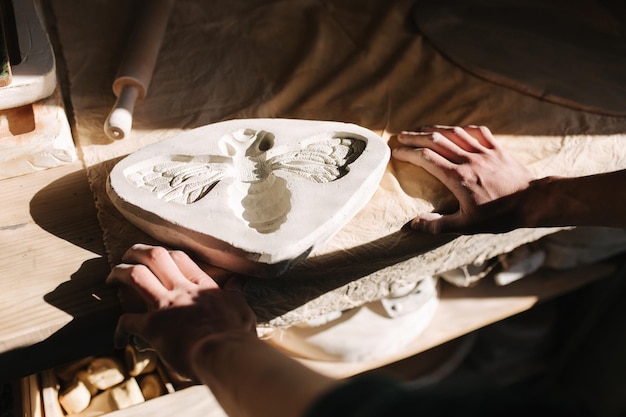 Ręce garncarza wypełniają formę ceramiką w kształcie motyla Zbliżenie dłoni