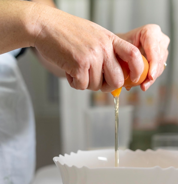 Ręce gospodyni domowej rozbijającej jajko w domowej kuchni, aby zacząć robić deser