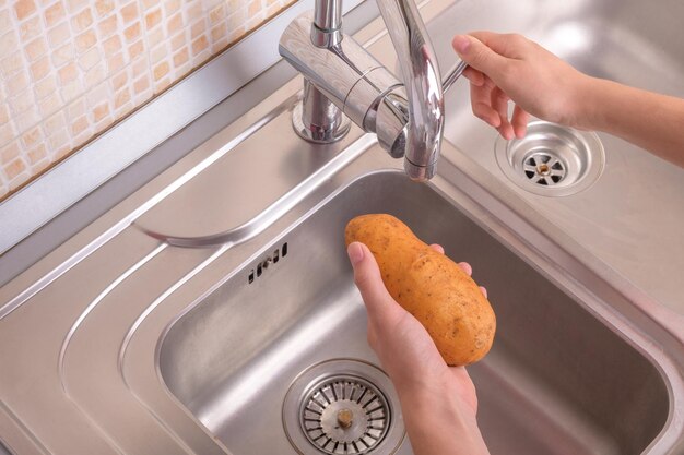 Ręce kobiet gotowe do mycia ziemniaków w zlewie w kuchni
