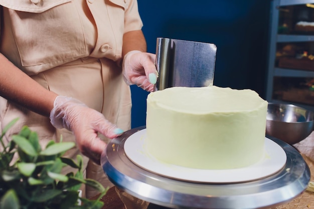 Ręce kobiet robią ciasto z białą śmietaną za pomocą spatuli do gotowania