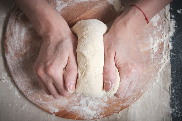 Ręce kobiet wyrabiają ciasto z mąki pszennej