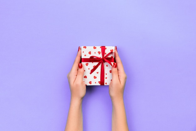 Ręce kobiety dają zapakowane walentynki lub inne ręcznie robione prezenty w papierze z czerwoną wstążką.