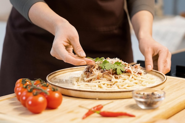 Ręce kobiety dekorujące górę gotowanego spaghetti z natką pietruszki