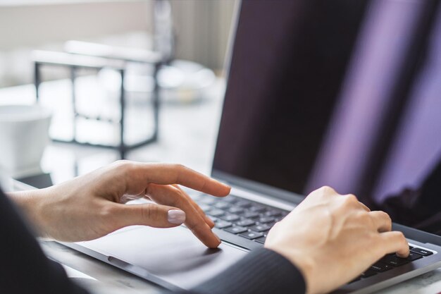 Ręce kobiety piszące na eleganckiej klawiaturze laptopa, a otoczenie biurowe wydaje się zamglone w tle