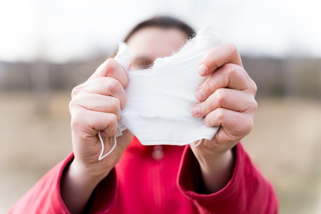 Ręce kobiety rozdzierają ochronną jednorazową maskę na twarz Koniec kwarantanny i samoizolacji z powodu pandemii covid19coronovirus Wyjdź z domu na ulicę Spaceruj na świeżym powietrzu na łonie natury