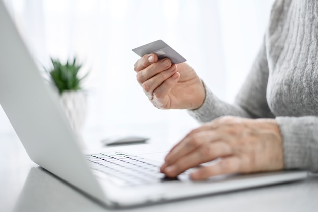 Ręce kobiety starszy pracy na laptopie z kartą kredytową przy użyciu nowoczesnych technologii w życiu codziennym. zakupy online.