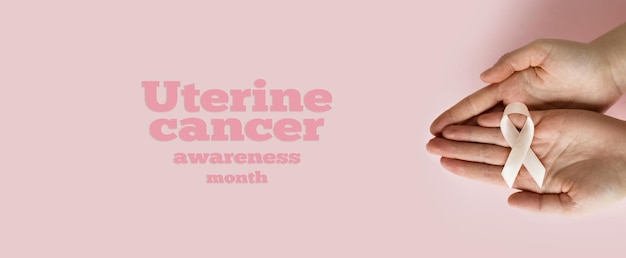 Ręce kobiety trzymają brzoskwiniową wstążkę na różowym tle Miesiąc świadomości raka macicy