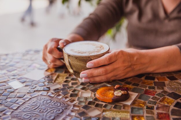 Ręce kobiety trzymają filiżankę kawy cappuccino na kolorowym szklanym stole w kawiarni