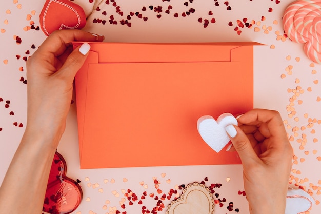 Ręce kobiety trzymającej list w kopercie rzemieślniczej na tle róży. Walentynki. Miejsce na tekst.