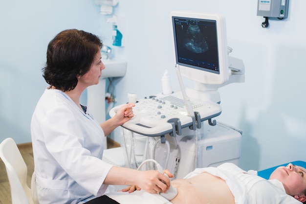 Ręce kobiety w ciąży i lekarz ze sprzętem USG
